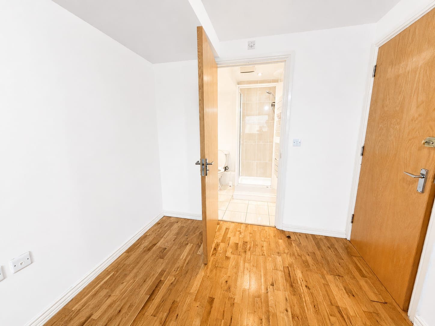 Spacious bedroom with warm wooden flooring, white walls, and direct access to ensuite bathroom. Light and airy space with ample storage.