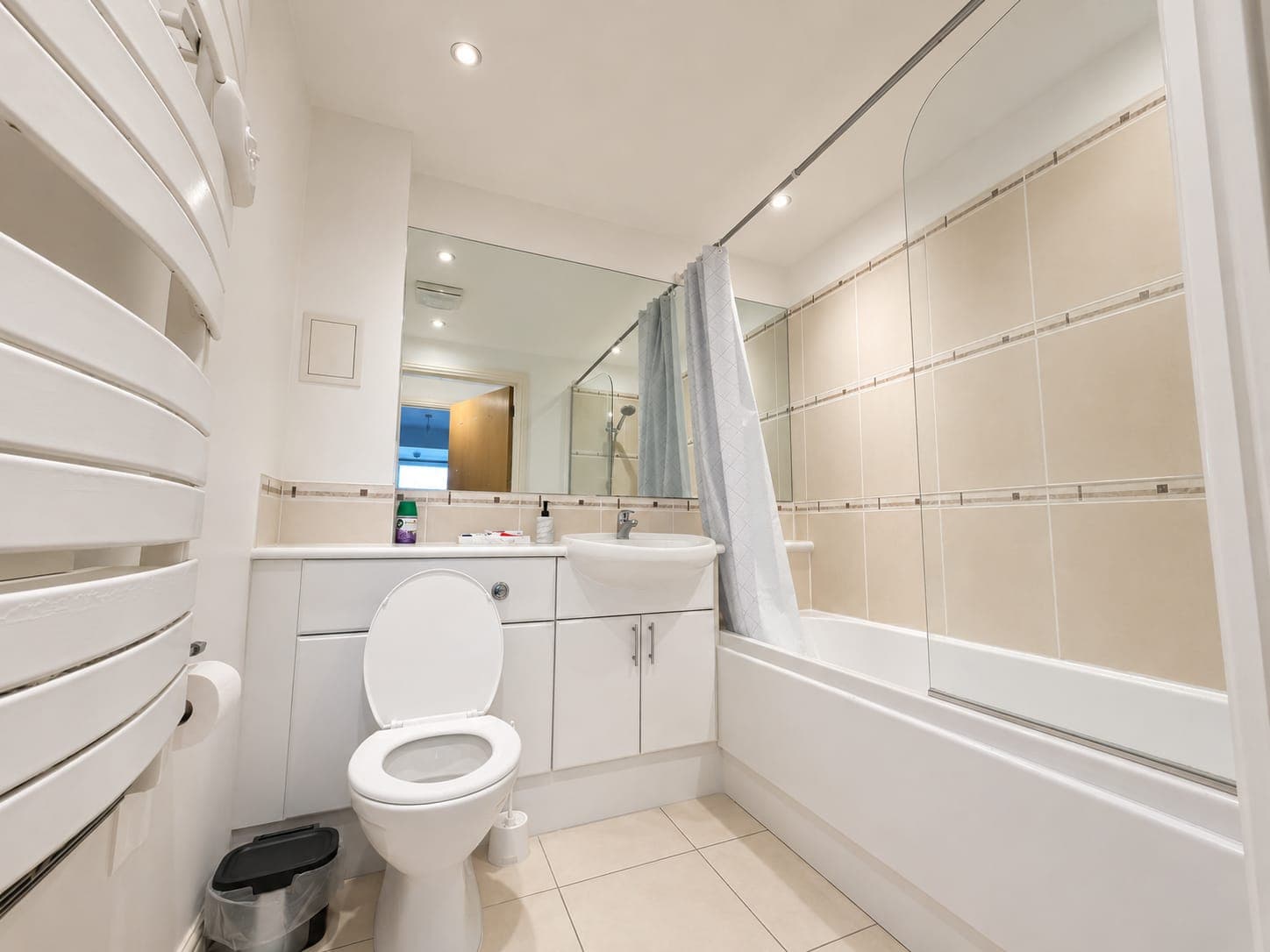 Modern en-suite bathroom featuring a walk-in shower with glass enclosure, white vanity unit with basin, toilet, heated towel rail, and bright recessed lighting throughout.